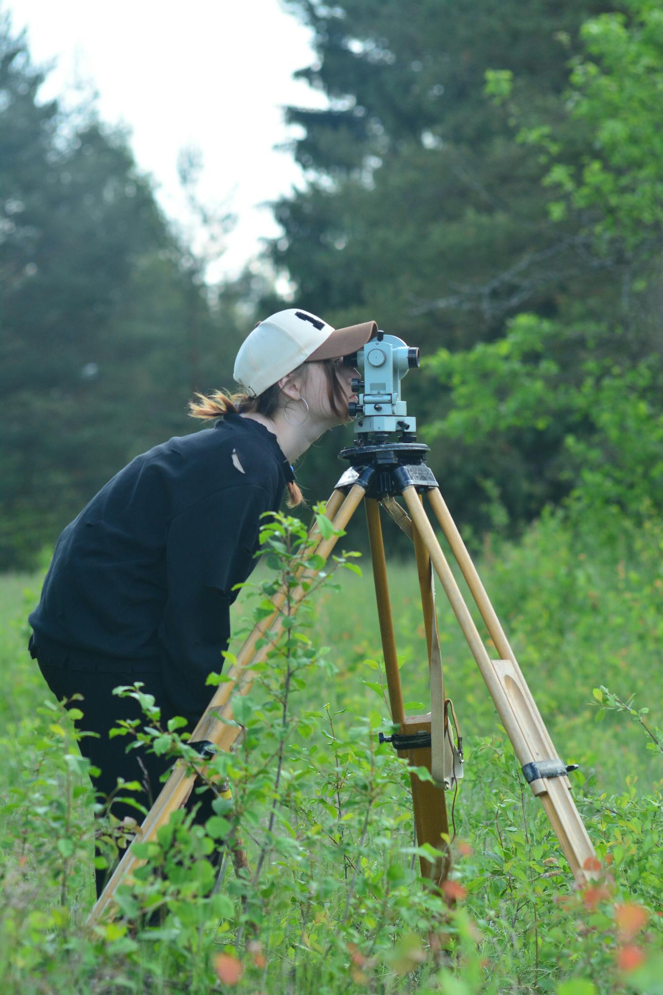 Surveyor using theodolite for measurements in outdoor forested area.